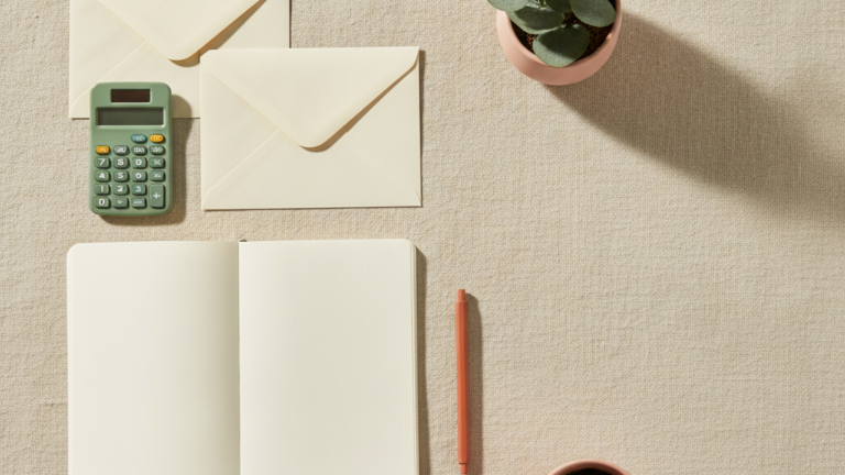 Two cream envelopes, a calculator, notebook and coffee on linen