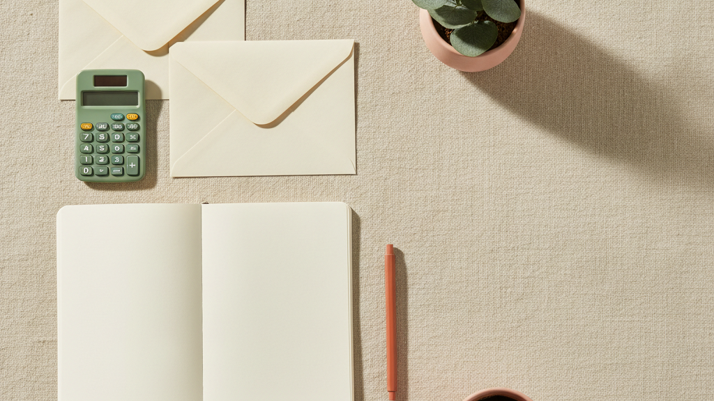 Two cream envelopes, a calculator, notebook and coffee on linen
