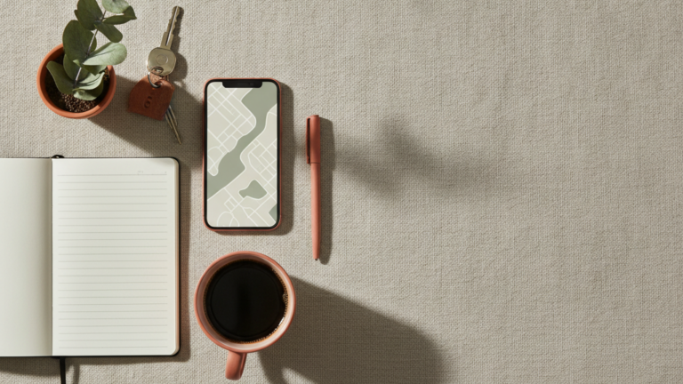 Car keys, an open logbook, a phone with a map, and coffee on linen